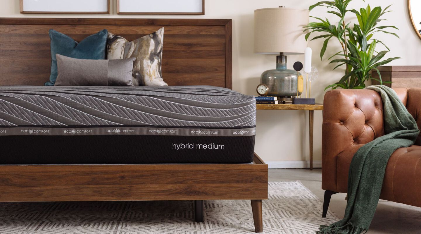 Black and grey mattress on a brown bedframe next to a brown leather chair