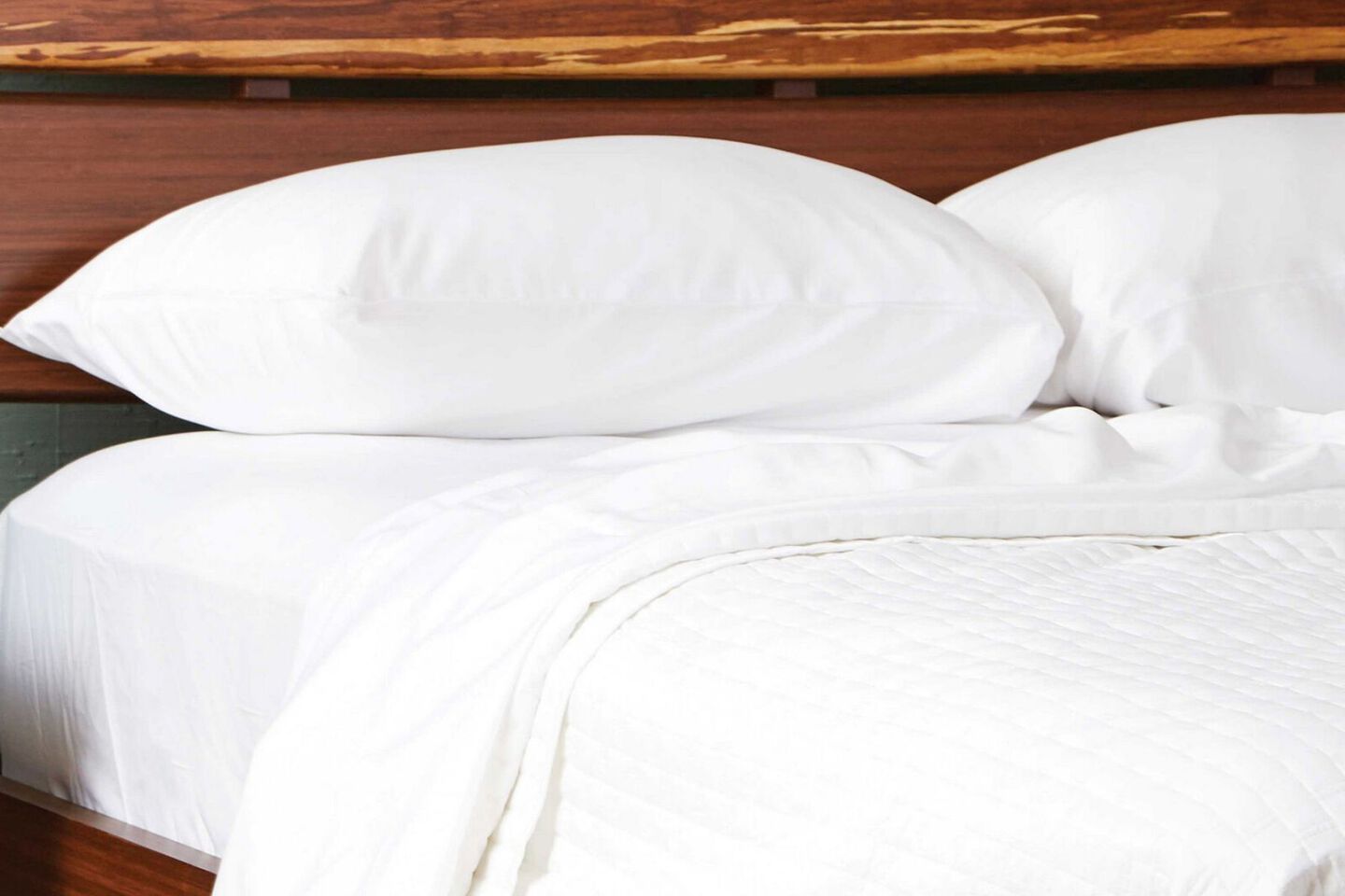Dark wooden bed with white sheet and pillows