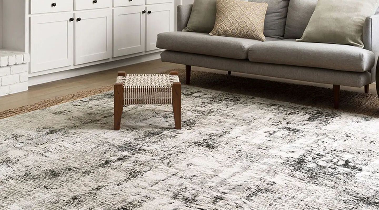 Living room with light grey couch, footstool, and grey and black rug