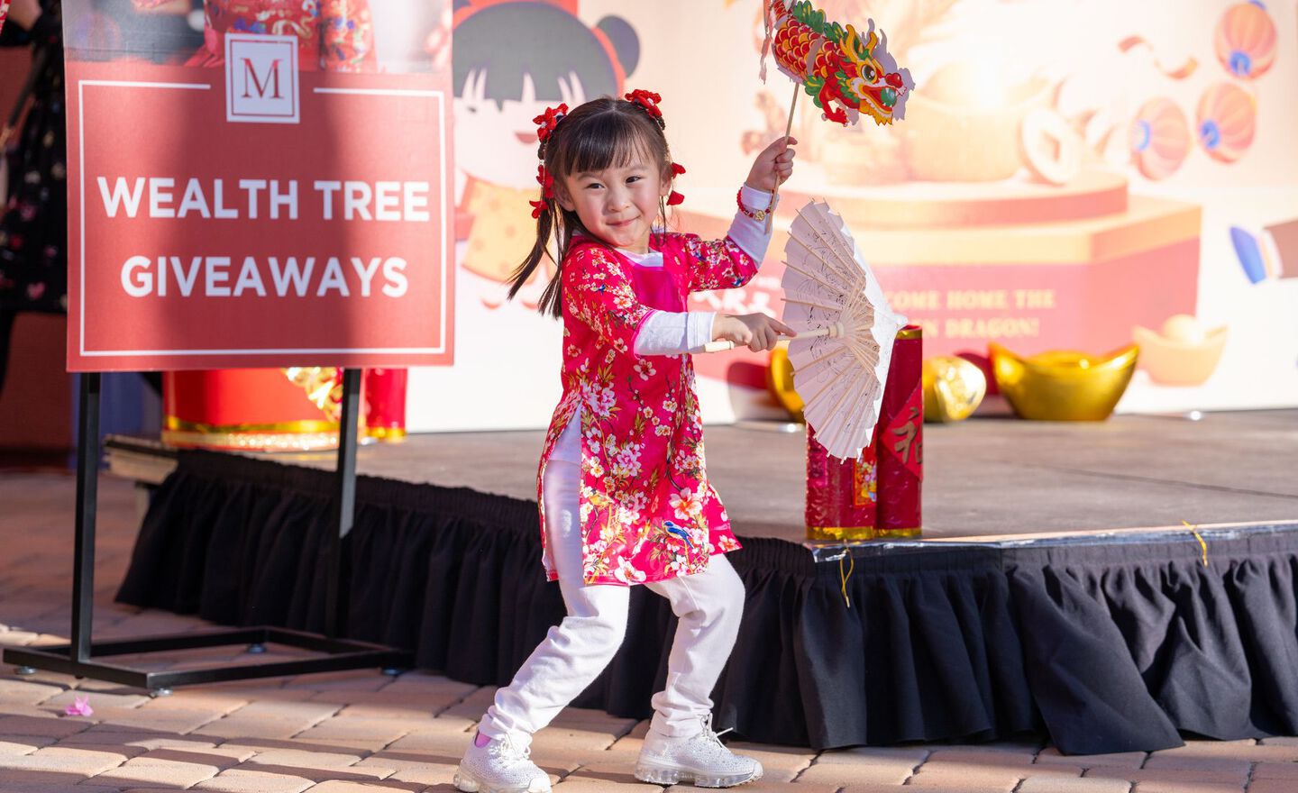 A small child posing in front of a stage with a paper dragon and paper umbrella