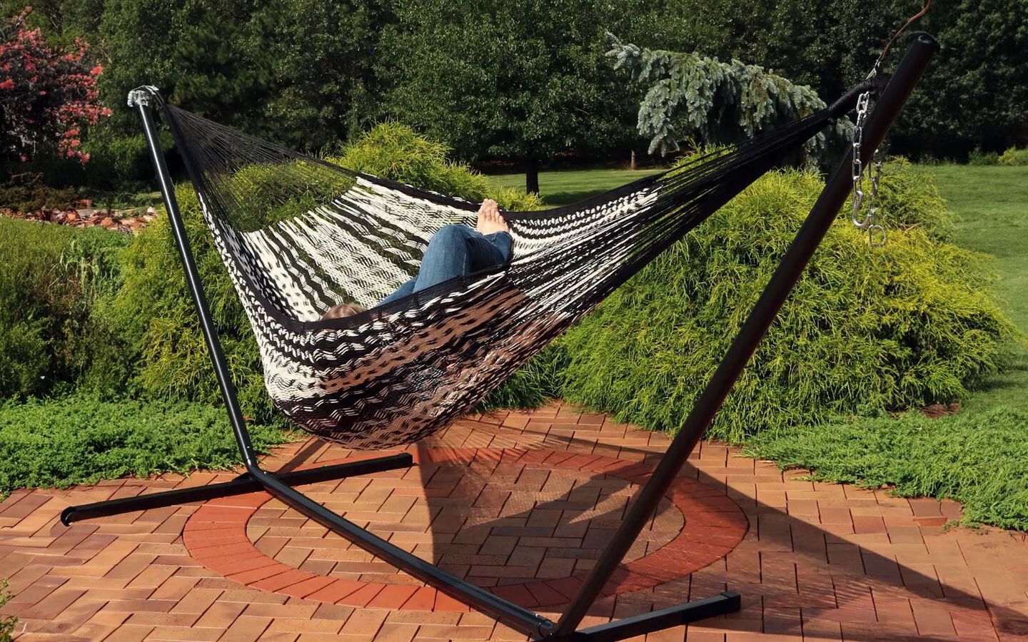 Person laying in a black and white knit hammock on a back patio
