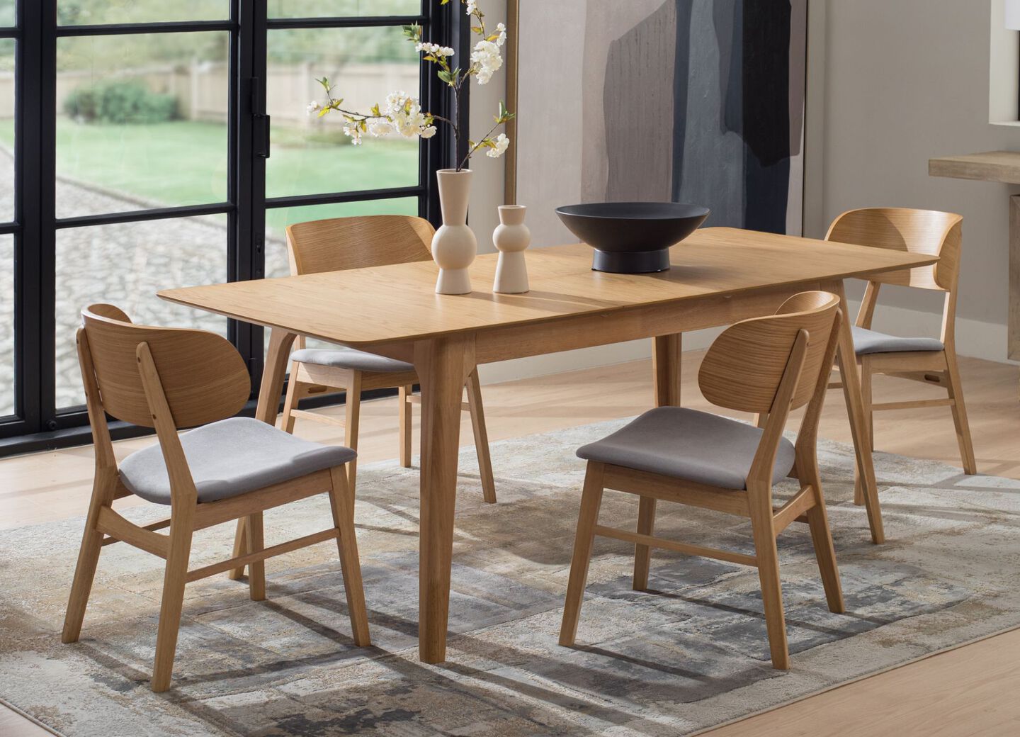 Light brown wooden kitchen table and matching chairs sitting on top of a grey rug.