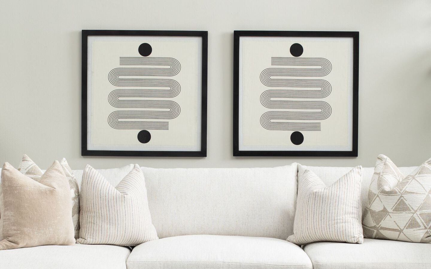 White couch with mixed pillows sitting below two framed pieces of artwork