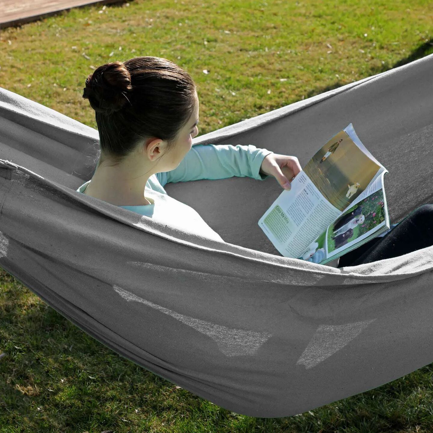 Girl sitting in a grey hammock reading a magazine