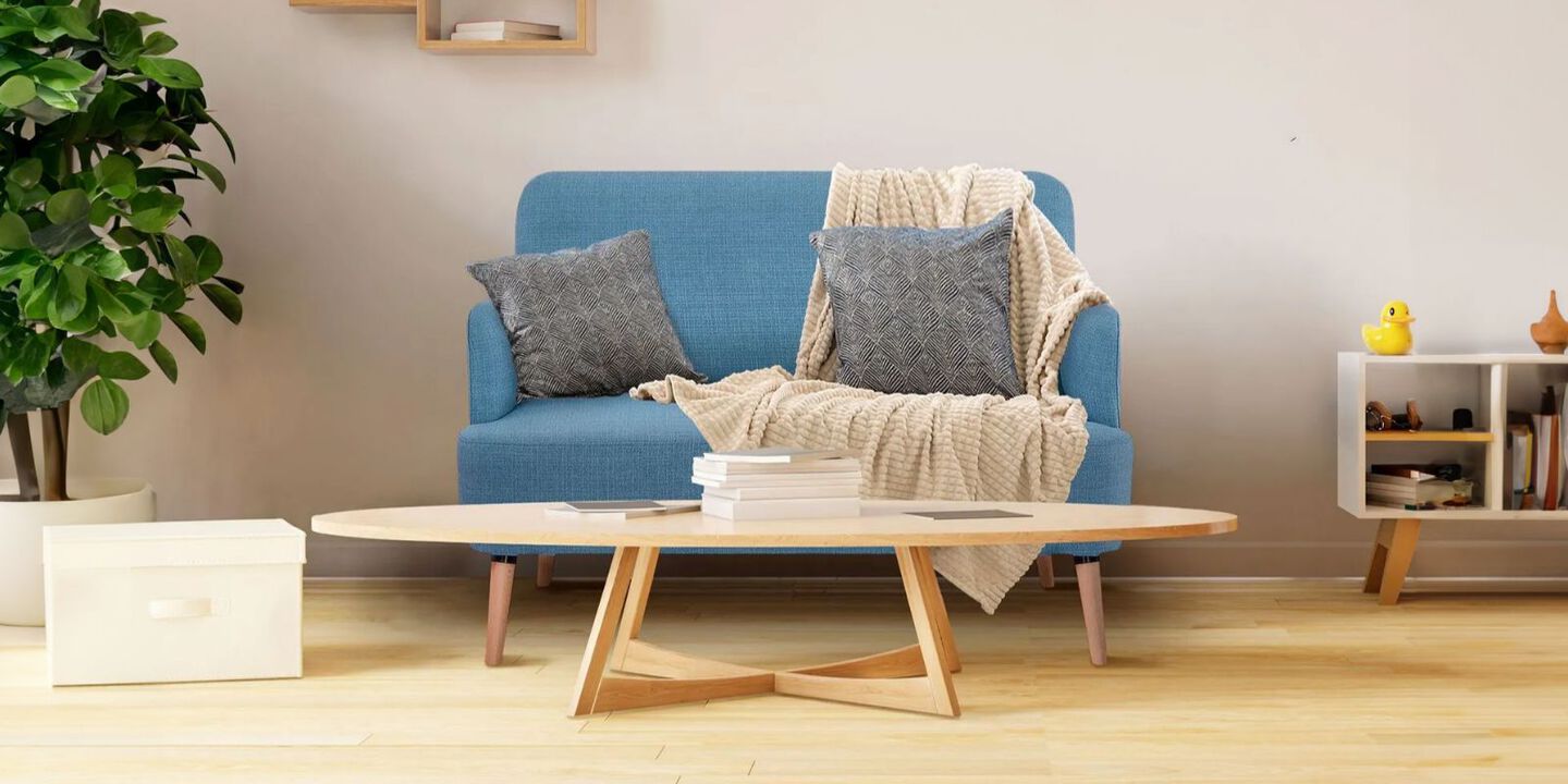 Living room with light wooden coffee table and small blue couch with grey pillows