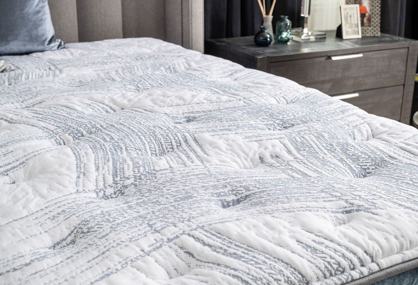 Closeup of a white and light blue mattress with a nightstand behind it