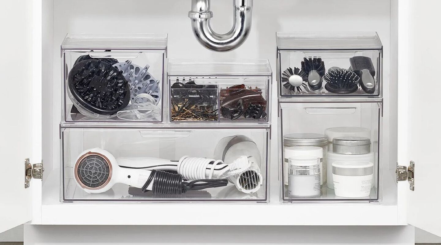 Plastic organization bins filled with supplies sitting in a cabinet below a sink
