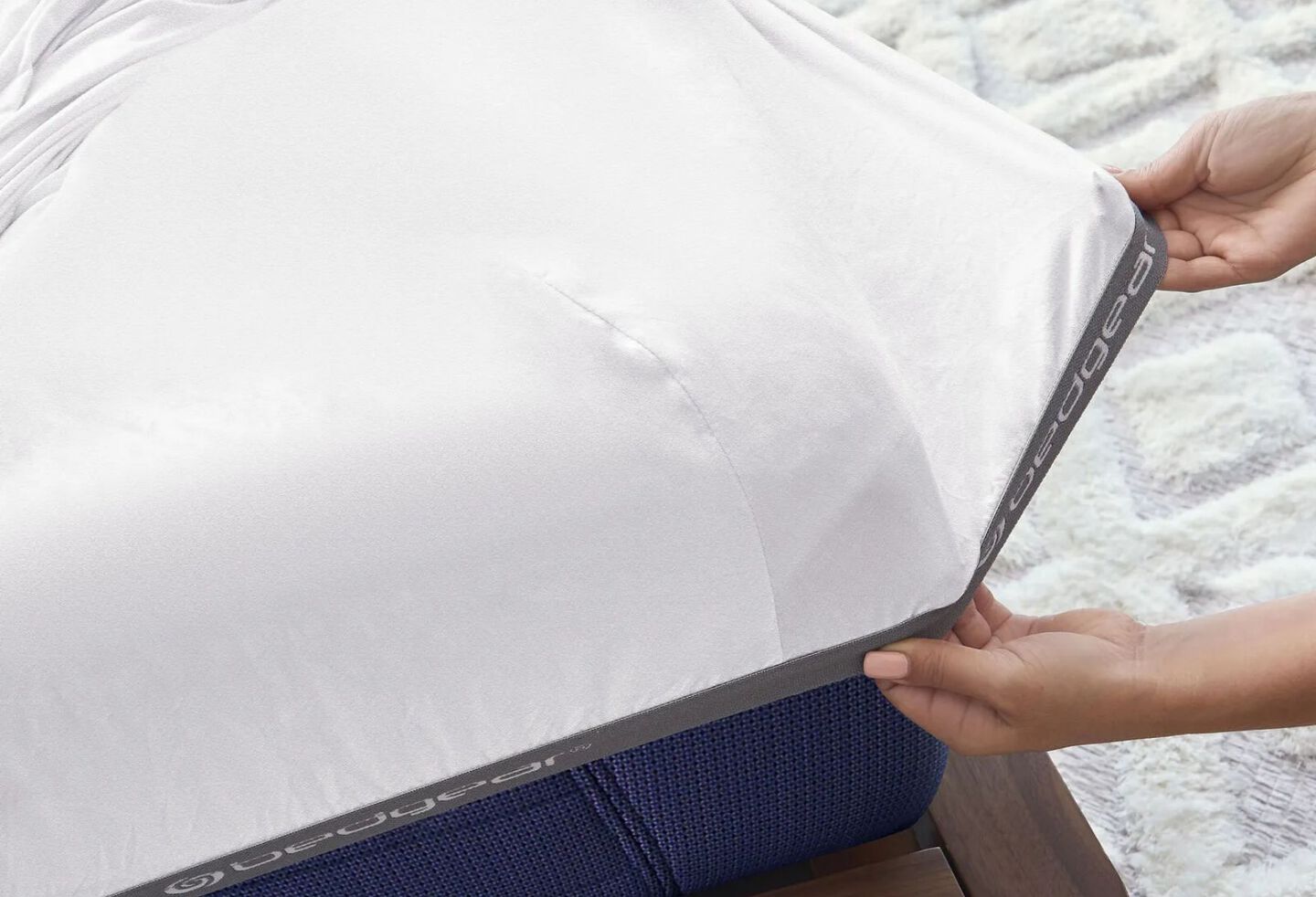 Closeup image of two hands pulling a sheet onto the corner of a bed