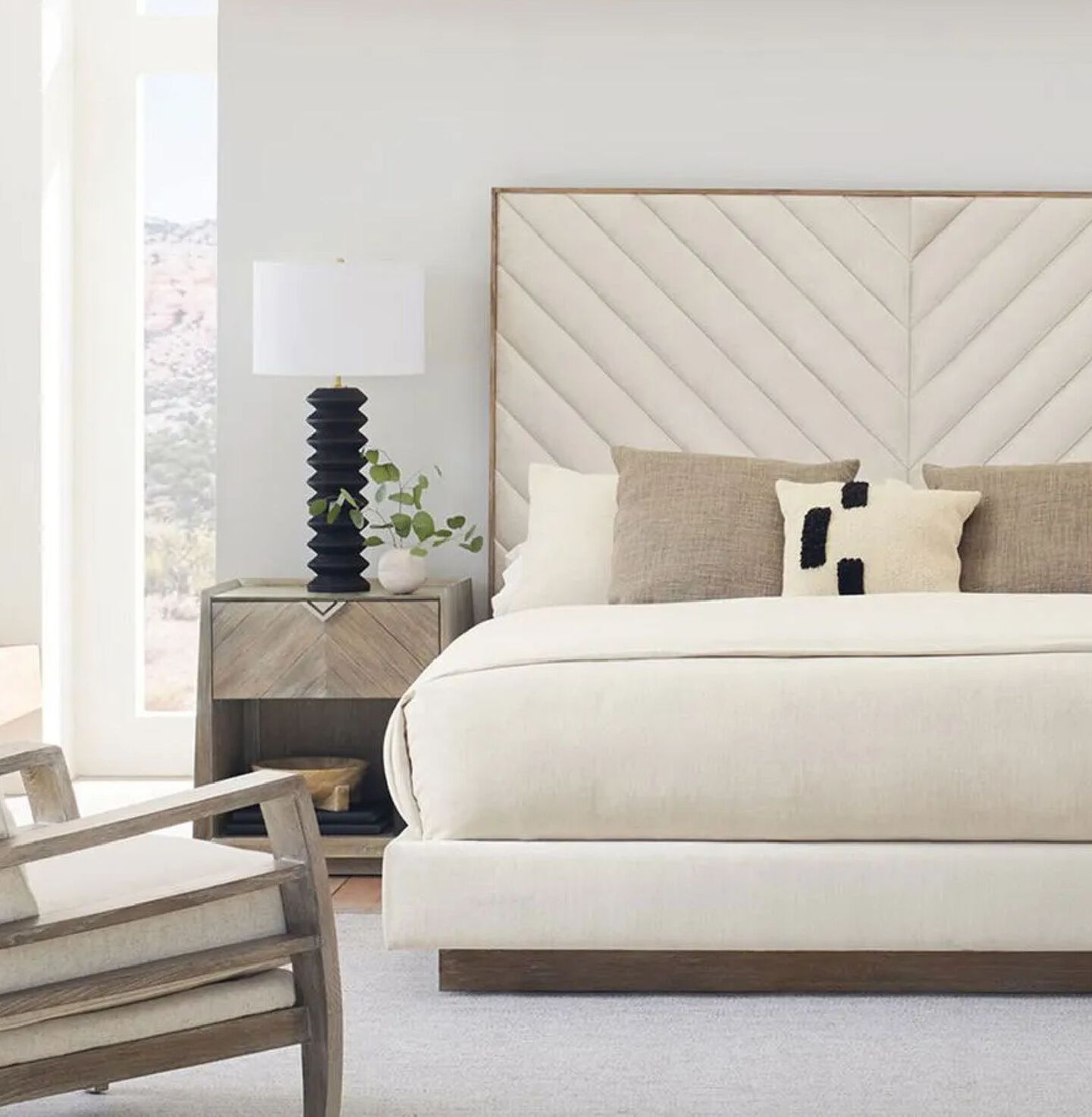 Bedroom with light brown nightstand and a cream colored bed with tan and white pillows