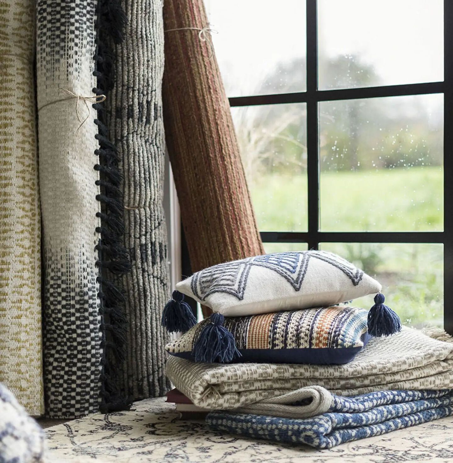 a stack of pillows and folded rugs sitting in front of four rolled rugs stood up behind them
