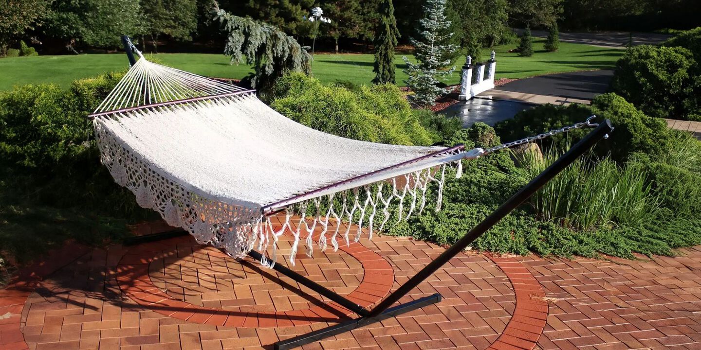 White knit hammock sitting on a red brick paved walkway in a backyard