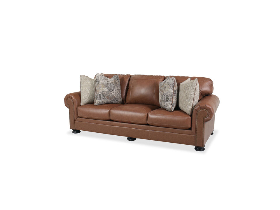 Brown transitional style Ashley leather sofa with rolled arms, nailhead trim, and four accent pillows