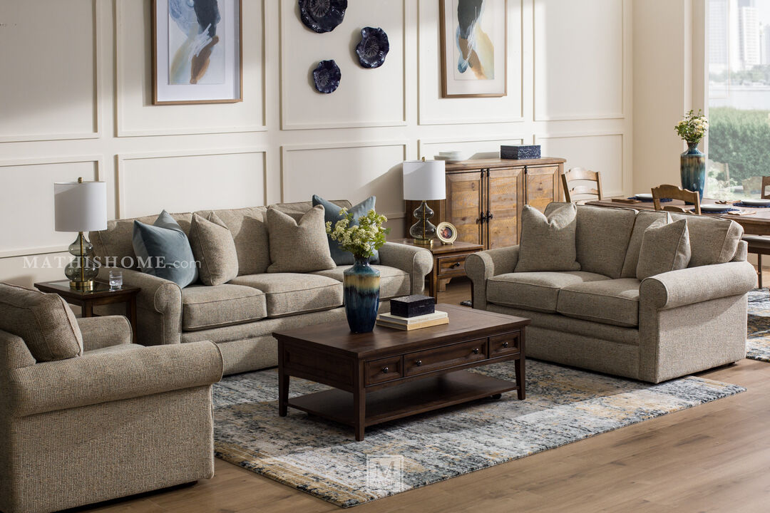 Three-seater sofa in a light gray textured fabric, featuring rolled arms and matching cushions. Accented with three plush pillows.