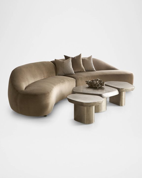 A unique, rounded sectional sofa with a smooth, velvety texture, complemented by a trio of sculptural side tables.